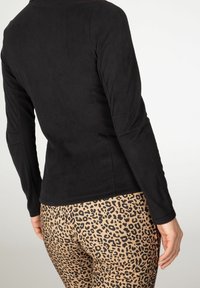 Top negro de manga larga con una textura suave, combinado con leggings beige ajustados que presentan un audaz estampado de leopardo negro.