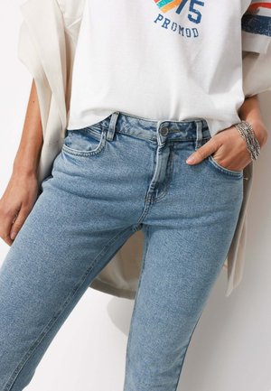 Jean en denim bleu clair à taille haute, doté de cinq poches, avec un léger délavage et une coupe ajustée. Associé à un t-shirt graphique blanc.