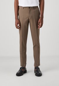 Pantaloni marroni su misura con una texture liscia, vestibilità slim, tasche laterali e chiusura a un pulsante. Abbinati a scarpe chiuse nere.