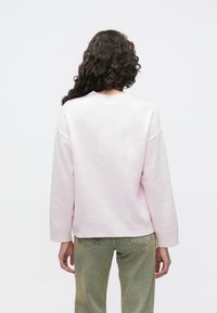 Svetlo roza majica z rahlim oprijetjem, rebrastimi manšetami in pasom. Narejena iz mehke tkanine, ima spuščena ramena in okrogel izrez.