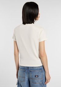 Crème korte mouwen t-shirt met een ronde halslijn. De stof is zacht en het heeft een getailleerd ontwerp, gezien vanaf de achterkant.