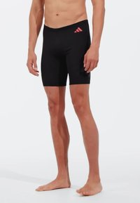 Bañador deportivo negro con un diseño ajustado. Presenta un logo rosa de Adidas en la cadera izquierda. Tejido suave, con una longitud hasta la mitad del muslo.