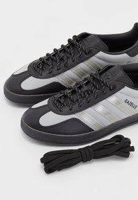 Black and gray athletic sneakers with synthetic upper, textured sides, and three silver stripes. Includes a rolled black shoelace.