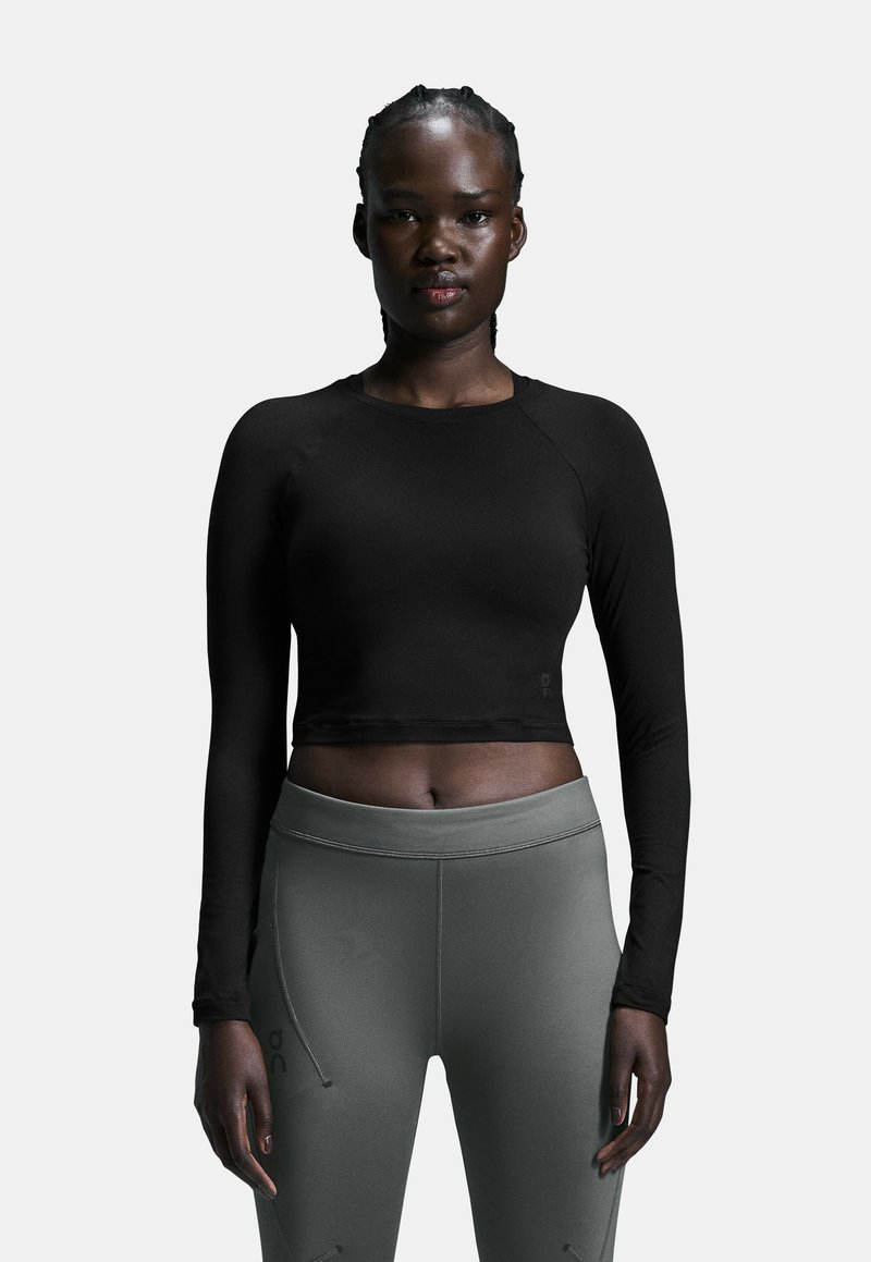 Schwarzes, langärmliges Crop-Top, kombiniert mit taillierten, dunkelgrauen Leggings. Das Top hat ein schlichtes Design; die Leggings besitzen Seitennaht und eine glatte Textur.