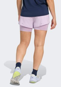 Lila hardloopshorts met gelaagd ontwerp, voorzien van een gladde textuur en reflecterende accenten. Draag ze met marineblauwe enkelsokken en witte sportschoenen.