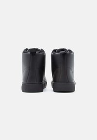 Mustad nahast pahkluu saapad tekstureeritud tallaga ja pehme voodriga. Tagaküljel on tõmbluku tõttu mugav selga panna. Minimalistlik disain, ilma nähtava brändita.