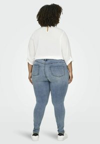 Top blanco ligero con abertura en forma de llave en la espalda, combinado con jeans ajustados de denim azul claro. Unas zapatillas blancas informales completan el look.