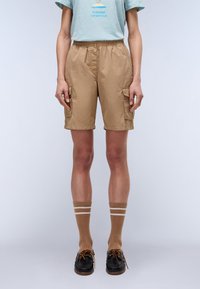 Shorts cargo beiges avec deux poches latérales, taille élastique et tissu léger. Associés à des chaussettes rayées marron et des chaussures bateau noires.