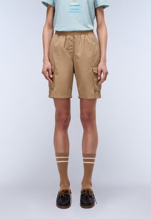 Beige cargo shorts med två sidofickor, elastisk midja och lättviktsmaterial. Matchas med bruna randiga strumpor och svarta båtskor.