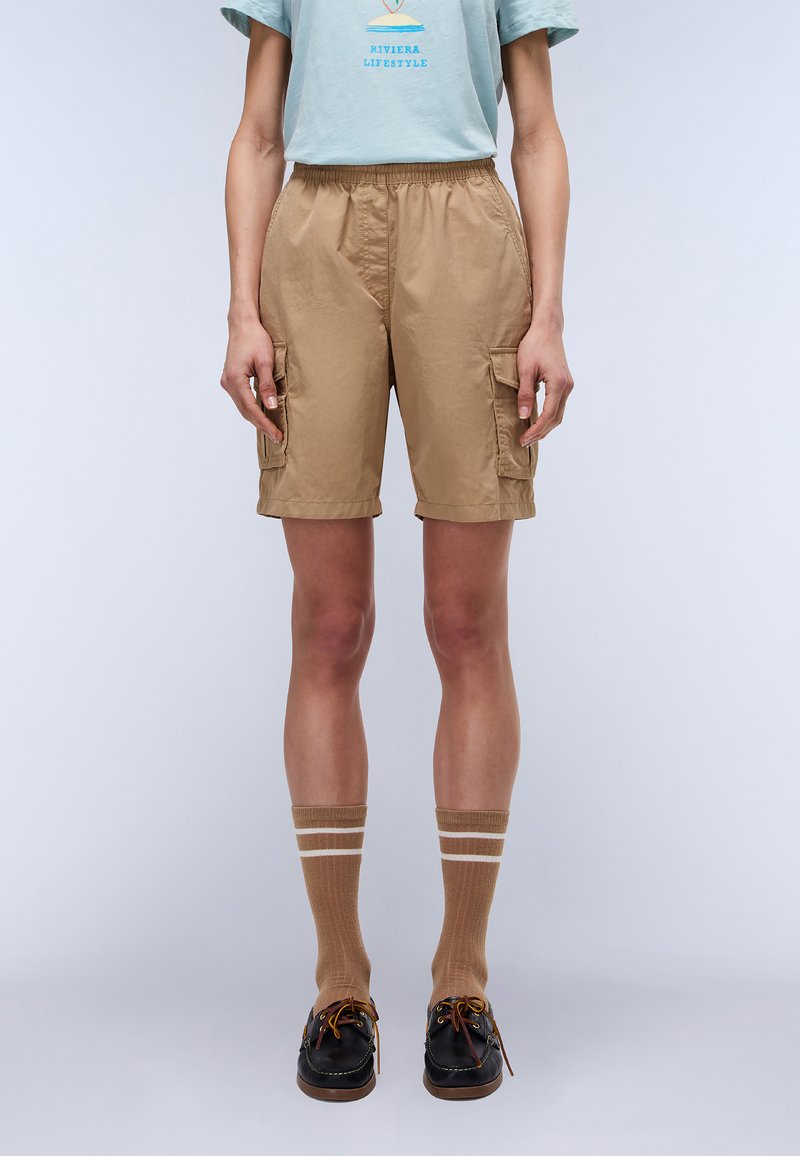 Shorts cargo beiges avec deux poches latérales, taille élastique et tissu léger. Associés à des chaussettes rayées marron et des chaussures bateau noires.