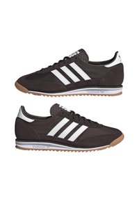 Scarpe sportive marroni con design a tre strisce bianche, tomaia texturizzata, suola in gomma e linguetta leggermente imbottita. Lacci piatti e dettaglio del logo.