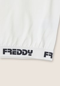 Tessuto bianco con un design arricciato sull'orlo, caratterizzato da una vita con logo "FREDDY" nero per un tocco in più. Texture liscia e stile semplice.