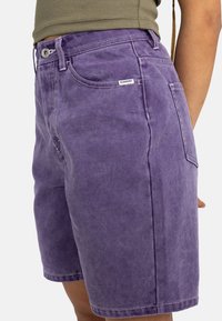 Pantaloni corti viola realizzati in tessuto morbido, con una vestibilità comoda, tasche standard e cuciture visibili. Etichetta del marchio attaccata sul retro.