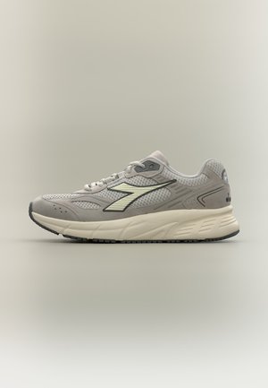 Chaussure de course grise et crème avec empeigne en mesh et suède, semelle épaisse et amortie, et logo stylisé sur le côté, présentée de profil sur fond neutre.