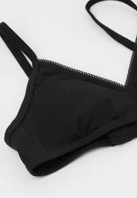 Černá podprsenka s tenkými ramínky a jemným krajkovým detailen. Vyrobena z měkké, pružné tkaniny s bezešvým designem a zapínáním na háček a oko.