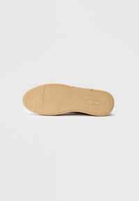 Suola di scarpa beige con modelli di presa testurizzati e logo "Lee" impresso vicino al tallone, mostrata su uno sfondo bianco.
