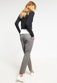 Grå byxor med en texturerad yta och framfickor, i kombination med en kort svart ribbad tröja och vita sneakers.