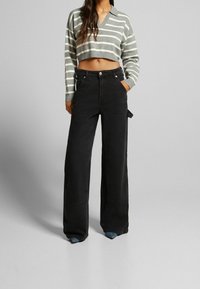 Pull cropped à rayures grises et blanches avec un col en V, associé à un pantalon large noir taille haute avec des poches avant.