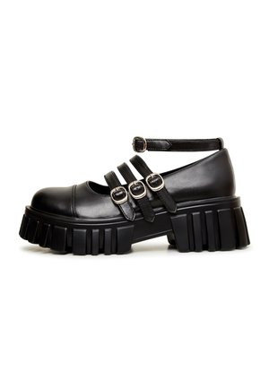 Chaussure noire à talons épais avec semelle plateforme épaisse. Comprend plusieurs lanières croisées avec des boucles métalliques. Texture en cuir lisse, bout arrondi.