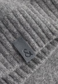 Graue gerippte Strickmütze aus weicher Wolle, mit einem rechteckigen, dunkelgrauen Stoffetikett mit Logo an der Seite.