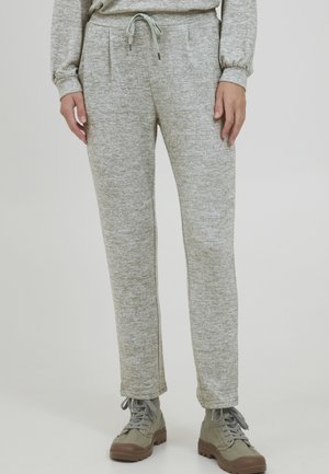 Graue Melange-Sweatpants mit einem Zugbandbund, seitlichen Taschen und einem tapered Beinschnitt, kombiniert mit olivgrünen Schuhen.
