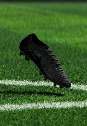 Črni nogometni čevelj lebdi nad zeleno travo blizu bele črte na nogometnem stadionu.