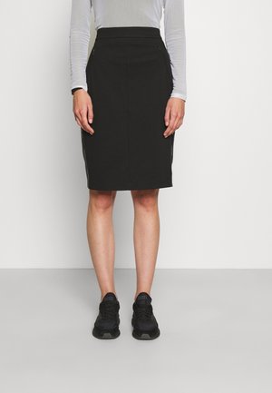 Jupe crayon noire à taille haute, avec des fermetures éclair sur le côté et une texture lisse. Associée à des chaussures de sport noires pour un look décontracté.