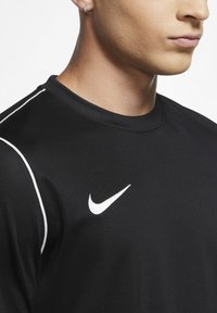 Camiseta atlética negra con el logo de la marca Nike en blanco, con un escote redondo y un ligero ribete blanco en los hombros. Textura suave.