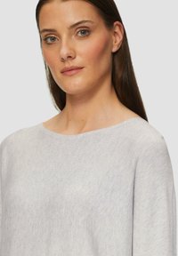 Lichtgrijze gebreide trui met een brede halslijn, lange mouwen en een zachte textuur, weergegeven op een neutrale achtergrond.