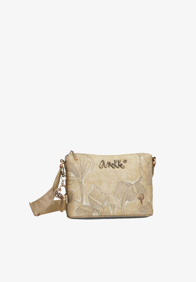 Sac à main beige avec un design floral embossé, logo en métal et une bandoulière amovible. Il dispose d'une fermeture zippée et d'accents en métal.
