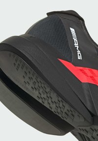 Sort atletisk sko med en struktureret overflade, rød detalje og en gummisål med riller, der har "LIGHT TRAXION" branding, designet til greb.
