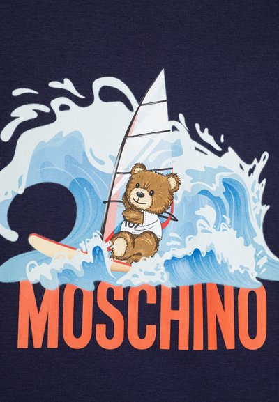 Camiseta azul marino con un oso de dibujos animados haciendo windsurf sobre una ola, con el texto "MOSCHINO" en naranja debajo. El diseño incluye patrones de olas en vibrantes tonos de azul y blanco.