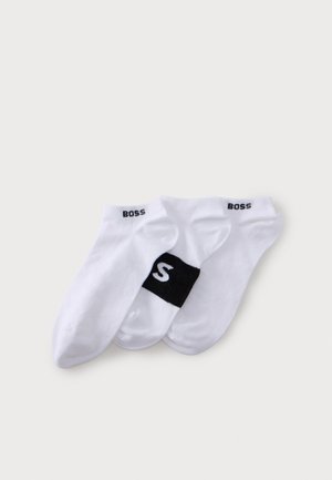 Trois chaussettes blanches à la cheville avec des logos BOSS noirs, disposées en se chevauchant sur un fond clair.