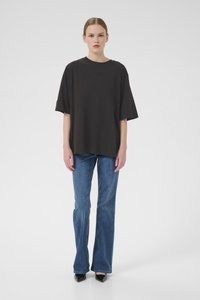 Zwarte oversized t-shirt met korte mouwen, ronde halslijn, met een subtiele logodetail. Gecombineerd met flared blauwe denim jeans en zwarte hakken.