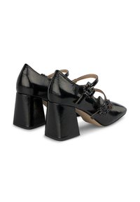 Zapatos de charol negro con tacones cuadrados y punteras afiladas, adornados con lazos decorativos en las correas frontales y un acabado liso y brillante.