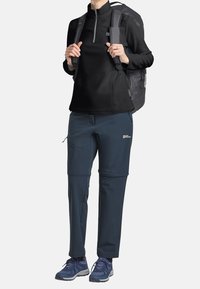 Czarna bluza z polaru z połową zamka, granatowe elastyczne spodnie z zamkami błyskawicznymi oraz szary plecak. Niebieskie buty trekkingowe. Funkcjonalny strój outdoorowy.