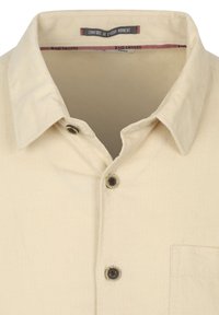 Beige overhemd met een kraag en een visgraatstructuur, voorzien van bruine knoopaccenten en een borstzak. Binnenlabel zegt "COMFORT BIJ ELK MOMENT."