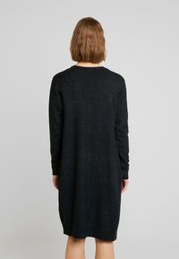 Robe noire à manches longues avec col rond, texture lisse, tombe au-dessus des genoux, avec des poignets côtelés et une coupe décontractée.