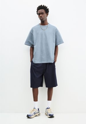 Lyseblå oversized t-shirt med kortærmer, parret med marineblå stribede shorts og grå træningssko. Tekstureret stof med en afslappet pasform.
