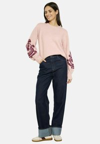 Svetlo roza pletena bunda z bordo cvetličnim vezenjem na rokavih, kombinirana s spletenimi temno jeans hlačami in debelimi kremnimi supergami.