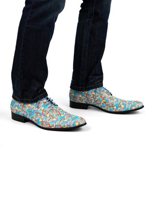 Kleurige, gepatternde schoenen met een blauwe basis, met intrikate bloemmotieven in roze, oranje en groen, gecombineerd met donkere jeans.