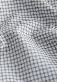 Tessuto bianco con motivo a quadri nero e grigio, che mostra pieghe morbide e texture.