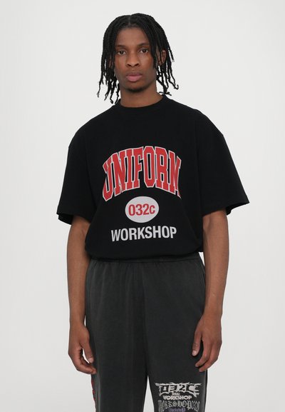 Black oversized t-shirt with "UNIFORM 032c WORKSHOP" in red and white lettering, paired with gray pants featuring graphic accents.