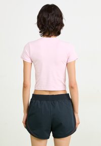 Pink cropped t-shirt with short sleeves, paired with black athletic shorts featuring a stretchy waistband and side mesh accents.
