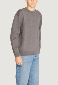 Maglione grigio lavorato a maglia con motivo a griglia, scollatura rotonda e polsini a coste, abbinato a jeans boyfriend blu chiaro.