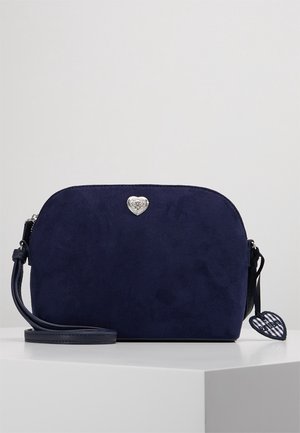 Petit sac bandoulière en daim bleu marine avec emblème cœur argenté et tirette de fermeture éclair en forme de cœur assortie sur une surface blanche.