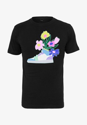Svart t-shirt med en färgstark grafisk bild av en sneaker med blommor, inklusive rosa, gula och blå blommor, mot en enfärgad bakgrund.
