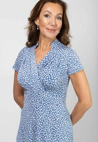 Niebieska sukienka w kwiaty z lekkiego materiału, z krótkimi rękawami i dopasowanym tależem, z małymi białymi wzorami kwiatów w całej powierzchni.