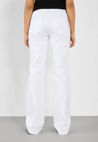 Jeans blancos acampanados con una textura suave, diseño de cinco bolsillos y cremallera en la parte delantera. Presenta una cintura alta y bolsillos traseros.