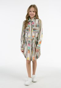 Abitino a camicia con maniche lunghe, fantasia colorata, chiusura a bottoni sul davanti, due tasche sul petto e una cintura di stoffa. Le sneakers bianche completano il look.